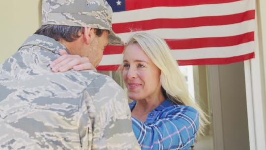 高加索男士兵在美国国旗上拥抱他微笑的妻子