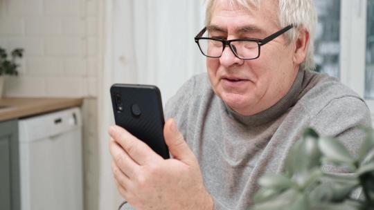 老人看着网络摄像头拿着电话与客户合作伙伴在线交谈