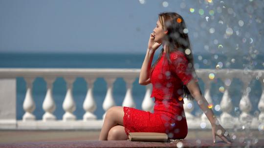 海边露台上穿着红色连衣裙的美女在打电话