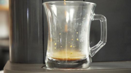 咖啡从家用胶囊咖啡机倒入玻璃杯，快进有趣的特写镜头