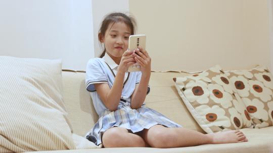 沙发上高兴的玩着手机的小女孩视频素材模板下载