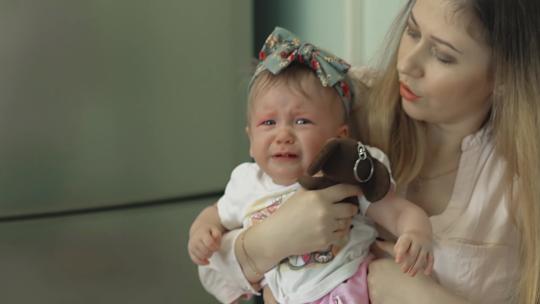 接种疫苗后，年轻美丽的母亲让女儿平静下来。女儿拿着一个毛绒玩具哭了。慢动作。
