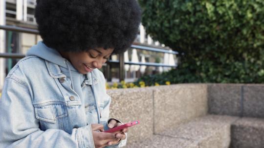 年轻的非裔美国妇女坐在户外使用手机
