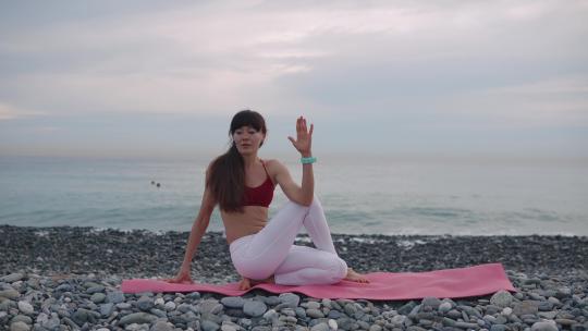 白天，一名运动女子坐在海边的卵石海岸上伸展身体视频素材模板下载