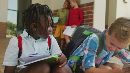 快乐的多样化男孩拿着书在学校前说话的视频