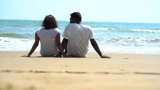 一对夫妇坐在海滩上面向大海的镜头