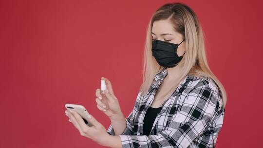 戴着口罩的女人在手机上喷洒消毒剂