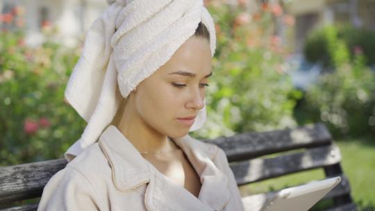 头戴毛巾穿着浴袍的年轻女子的肖像坐在长凳上时得到了令人震惊的消息