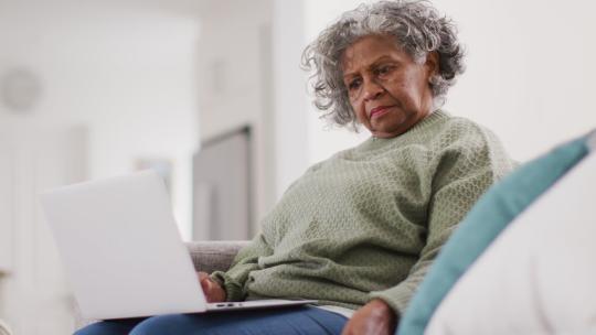 高级非裔美国妇女坐在沙发上，使用笔记本电脑和智能手机的肖像视频素材模板下载