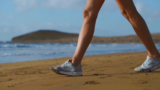 一个穿着白色运动鞋的女人走在海滩上的特写镜头，美丽的白沙