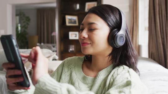 深色头发的微笑混血女人使用耳机和智能手机的视频