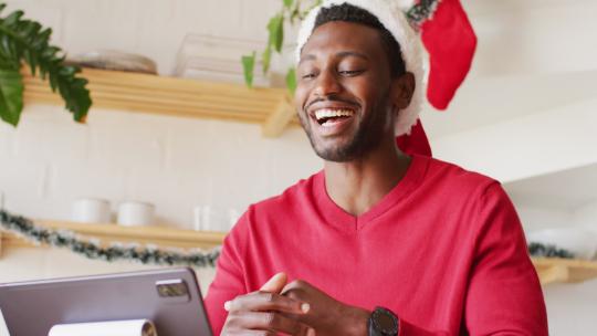 快乐的非裔美国人戴着圣诞帽，使用平板电脑进行视频通话