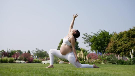 夏日清晨怀孕美女在公园草地练瑜伽锻炼健身