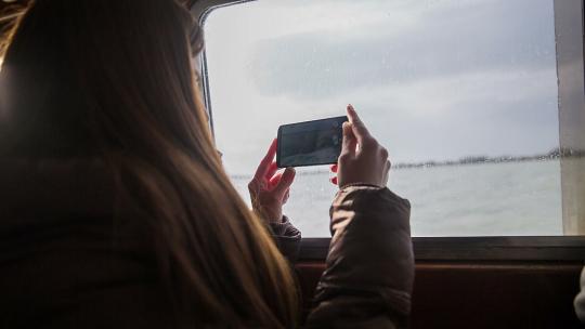 女人在船上记录周围的环境。阳光明媚的一天，带着漂亮的长指甲和大智能手机在海景外拍照和录像的女性在海上乘船旅行。