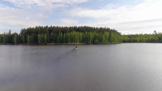 鸟瞰被森林包围的湖泊，两名渔民在船上捕鱼