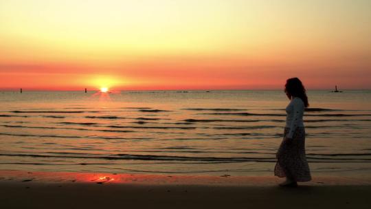 日落时走在海滩上的女孩