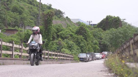 一名女子骑着一辆小摩托过桥