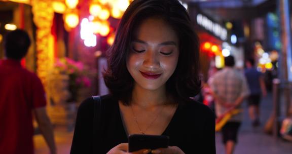 美女在夜晚城市街头看手机
