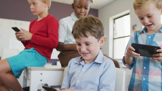 不同男孩坐在学校课桌前用智能手机玩游戏的视频