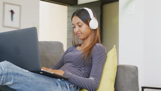 一个带着耳机的混血少女在家用笔记本电脑，慢动作视频素材模板下载