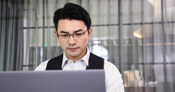一个商务男士坐在办公桌前使用电脑