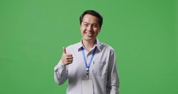 一个亚洲商人在绿屏工作室里竖起大拇指，微笑着