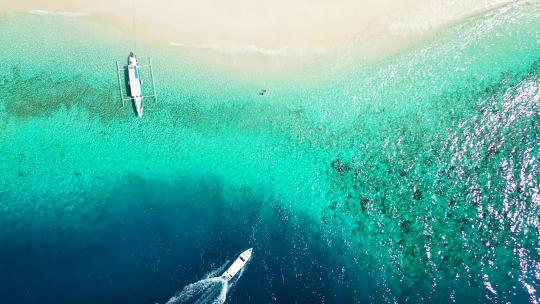 游船在深蓝色的大海中追踪和起泡，驶向附近的浅水绿松石泻湖视频素材模板下载