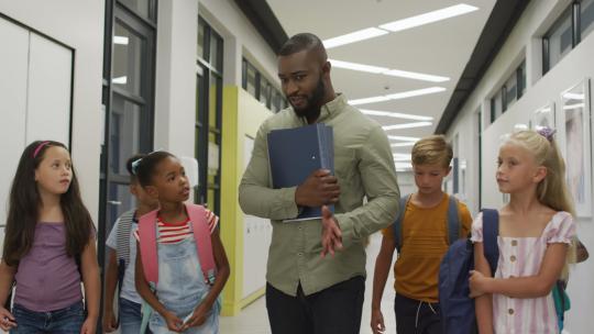 快乐的非裔美国男教师和不同学生在学校大厅散步的视频