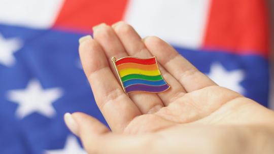 年轻女子手里拿着同性恋、双性恋和变性者的图标。背景是美国国旗。