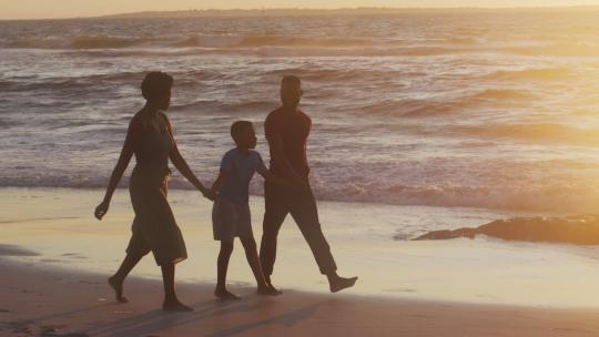 日落时分快乐的非裔美国家庭在海滩上散步的视频