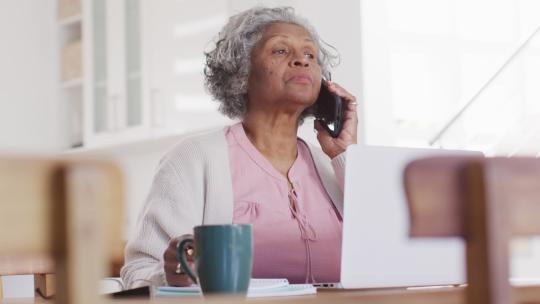高级非裔美国妇女坐在桌旁，使用笔记本电脑和智能手机交谈的肖像视频素材模板下载