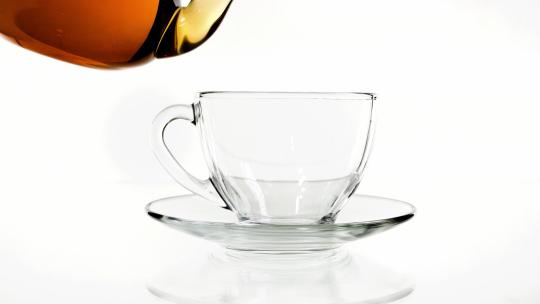 在白色背景前将茶倒进透明玻璃茶杯