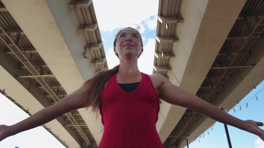 一名穿着红色训练服的成年女子站在桥下双手合十