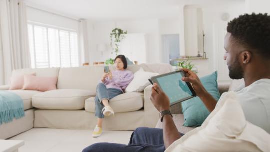 不同的夫妇坐在沙发上，在客厅里使用平板电脑