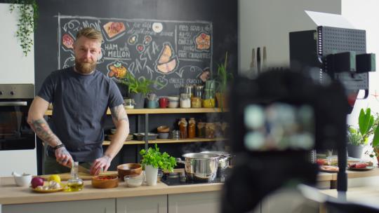 男厨师在厨房餐桌上切菜，在为美食博客拍摄烹饪课时在镜头前讲述食谱