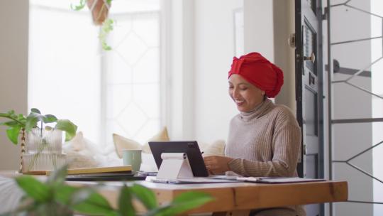 戴头巾的快乐混血儿女人坐在办公桌前在家打平板电脑视频电话的视频，复制空间