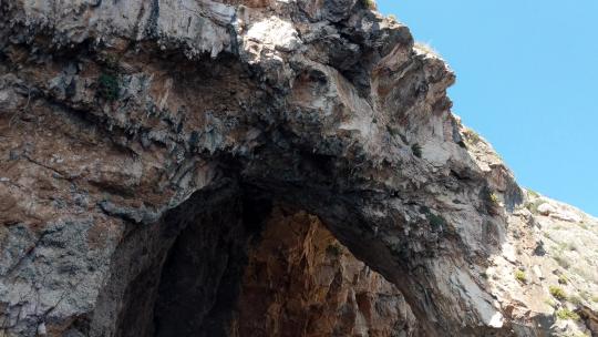 在阳光明媚的夏日，传统的luzzu渔船在马耳他蓝色洞穴的岩石洞穴下航行
