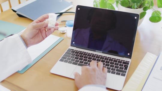 高级混血男医生使用笔记本电脑和持有药物，在屏幕上复制空间