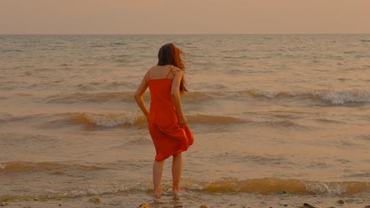 晚间夕阳下波浪拍岸的海边美女背影