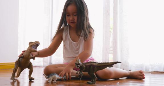 小女孩坐在地板上玩恐龙玩具