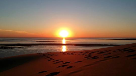 无人机视频拍摄了一个美丽的橙色日落，沙丘上有大海背景，沙子上有脚印