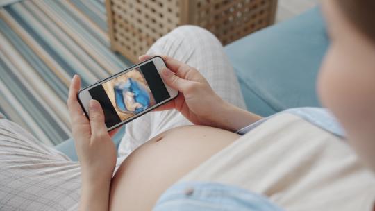 孕妇使用智能手机观看子宫内婴儿视频素材模板下载