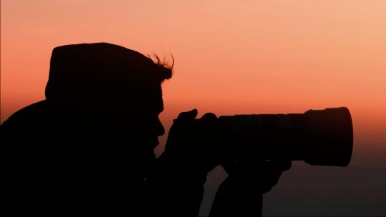 夕阳下拿起相机拍照的男人·剪影视频素材模板下载