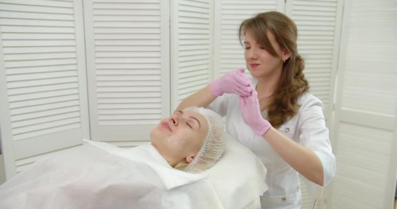 美容师在美容诊所的一个年轻漂亮女人脸上涂抹面霜。