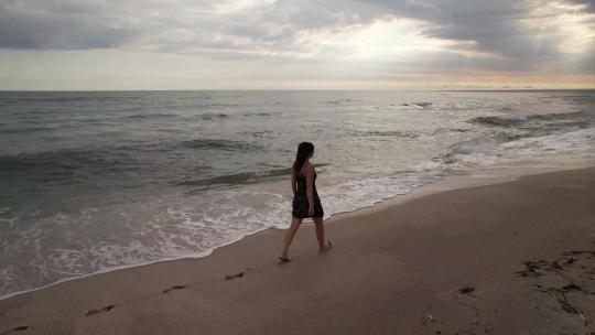 女孩在沙滩上行走，她的脚被大海冲刷
