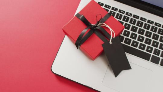 笔记本电脑和带黑色丝带和礼品标签的红色礼品盒，红色背景，带复制空间