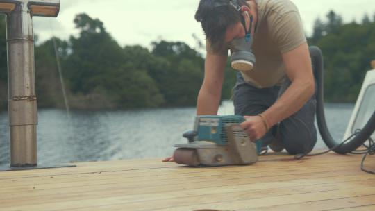 木匠使用皮带砂光机打磨木船屋顶。中等关闭
