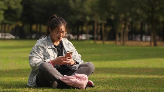 大学生活 女孩盘腿坐在校园草地上看手机