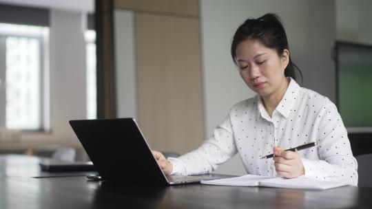 职业女性在电脑上工作，用笔记录