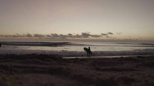 日落时的海边的冲浪者散步